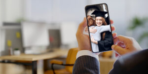 A businessman at work looking at a photo of his daughter's college graduation on his cellphone